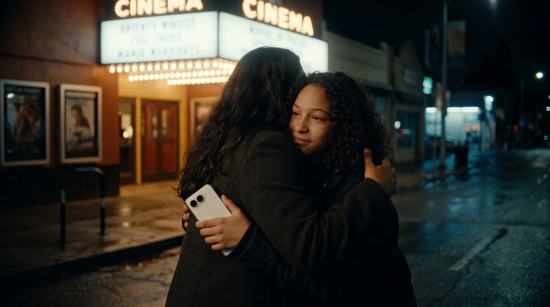 Two friends embracing outside a cinema at night