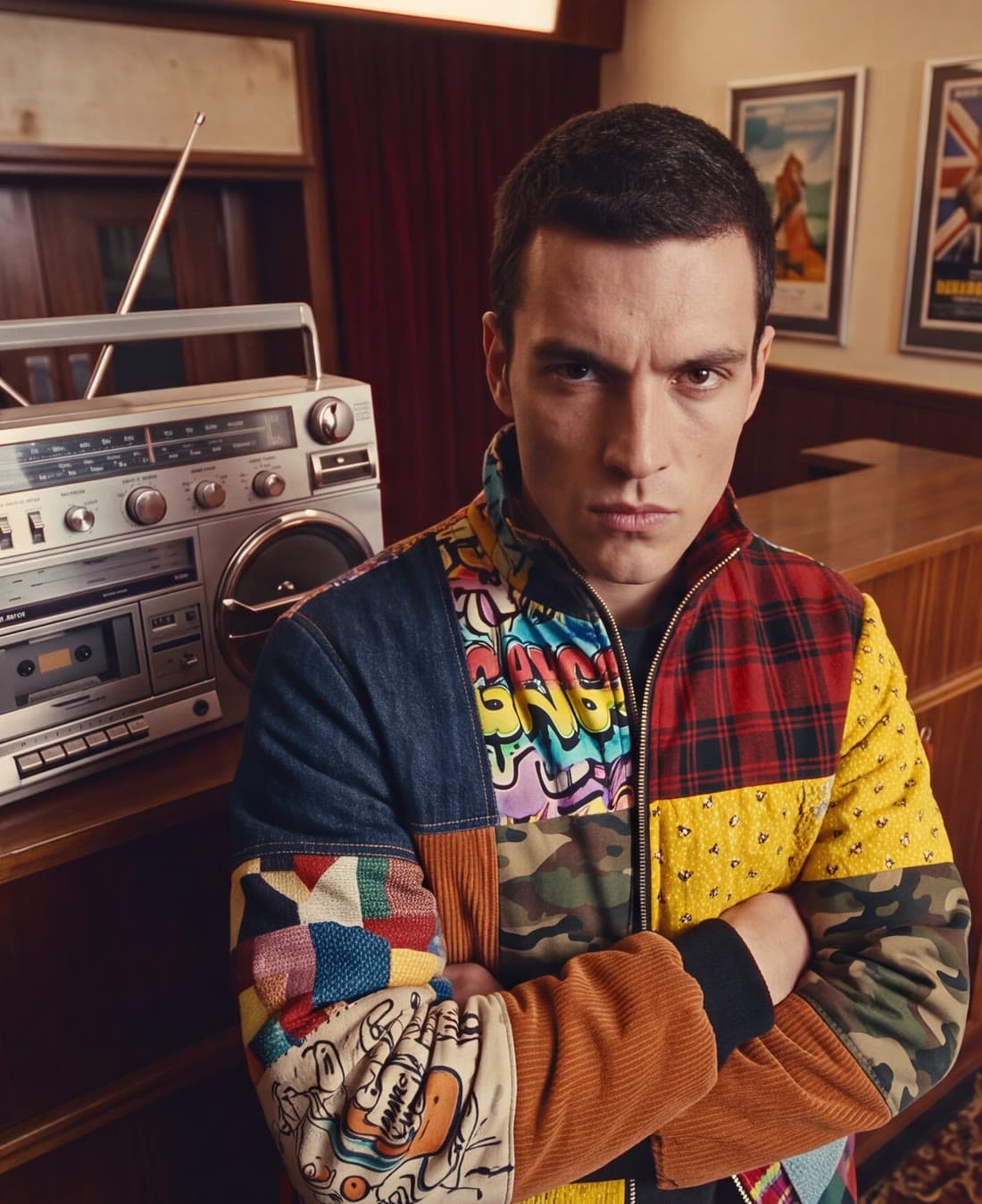 A man in a patchwork jacket beside a boombox in a cinema lobby
