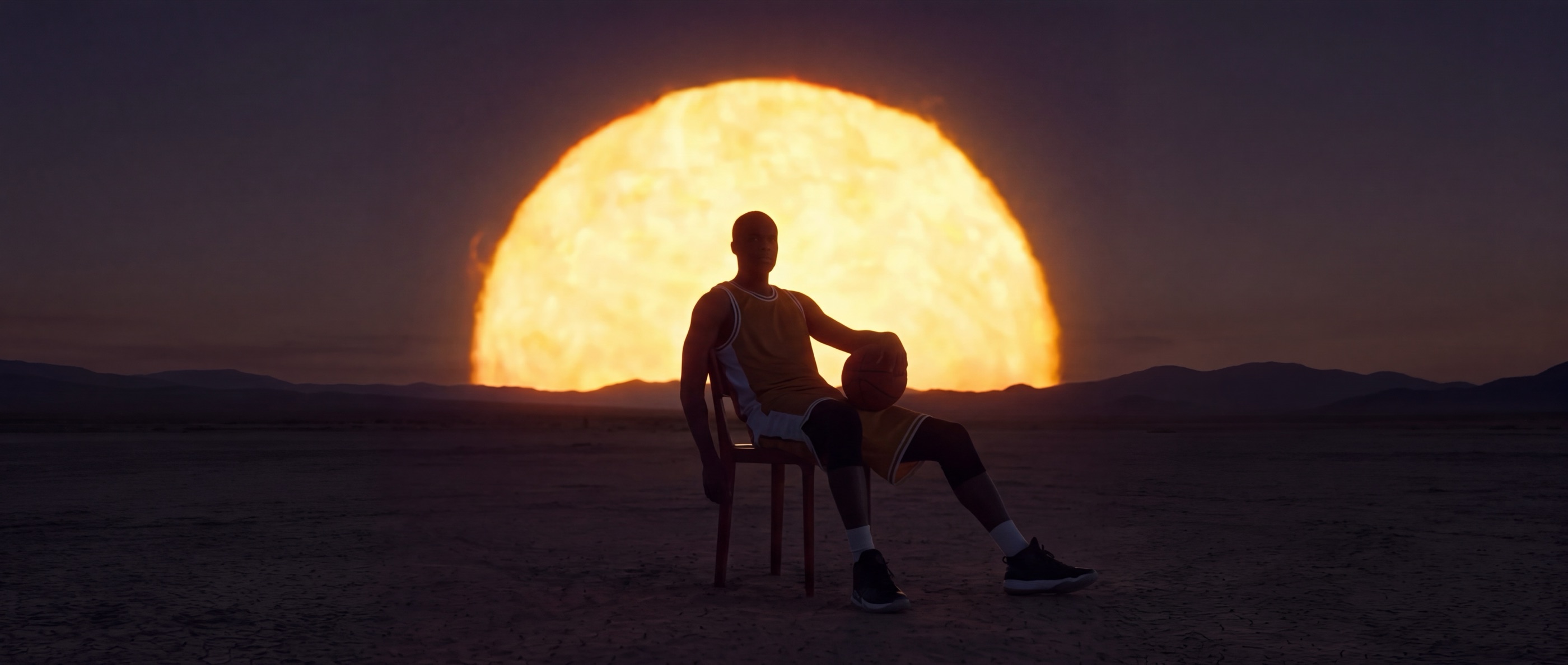 A basketball player seated in the desert before a giant setting sun